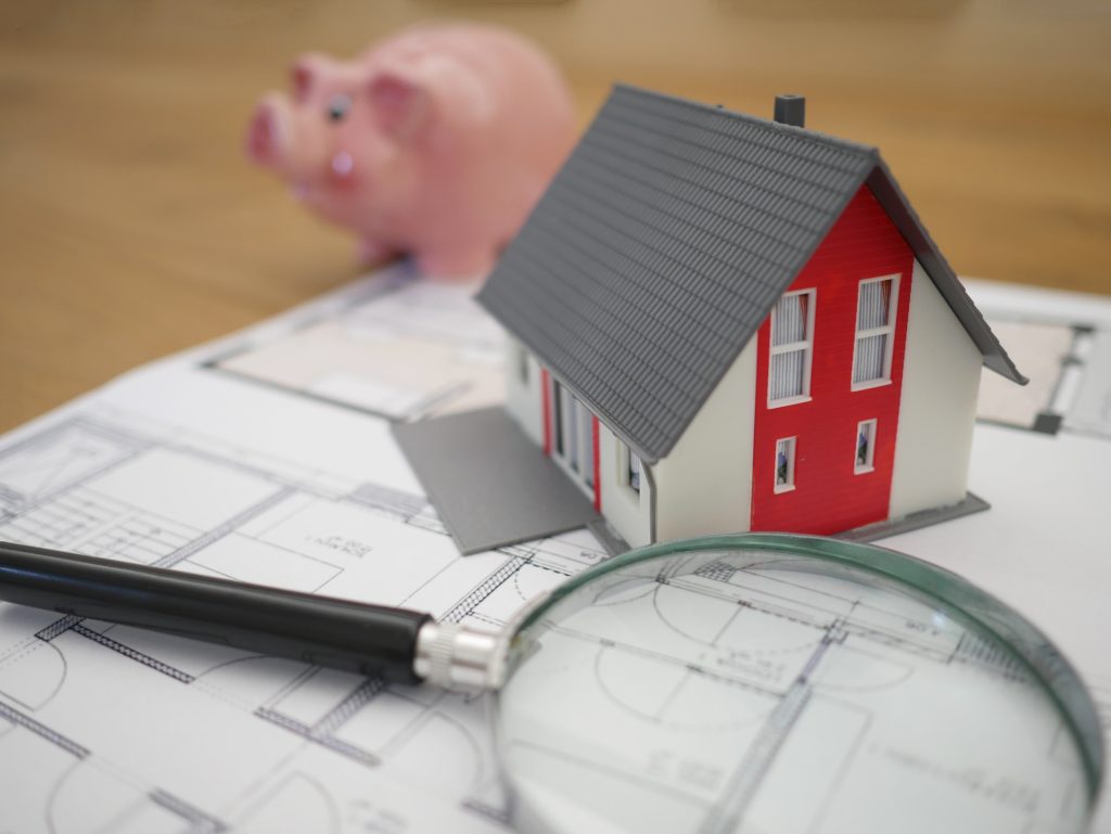 home blueprint with magnifying glass and piggy bank