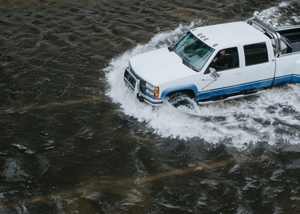 person in a truck driving through flood waters